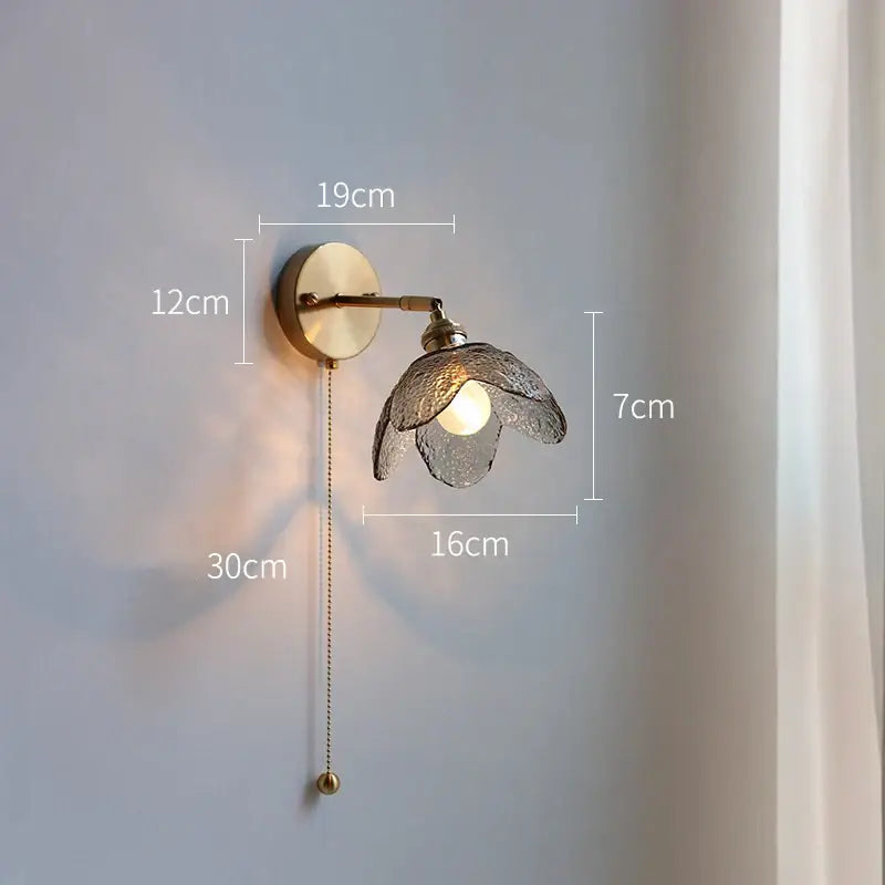 A brass flower gray glass led wall lamp with textured translucent shade and adjustable pull chain for bathroom use