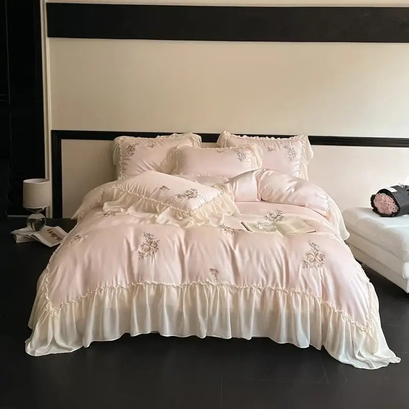 A delicate blush pink satin lyocell bedding set with cream flowers embroidery and lace ruffles for elegant decor