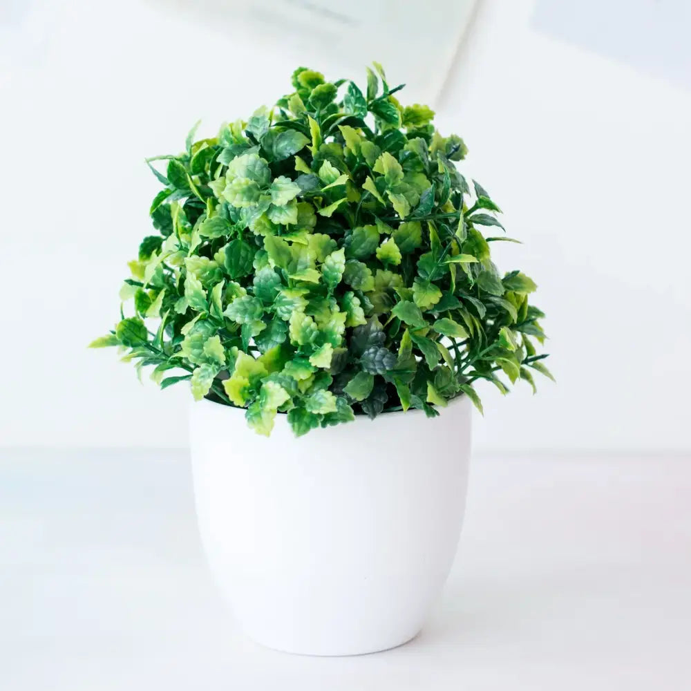 A lush decorbites artificial mini plant bonsai with varied green leaves in a white ceramic pot for desktop decor