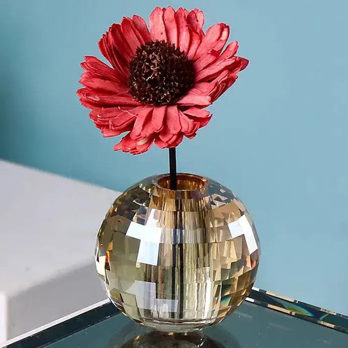 A faceted gold crystal ball aroma diffuser with a geometric base holding a vibrant red dried flower for bedroom decor