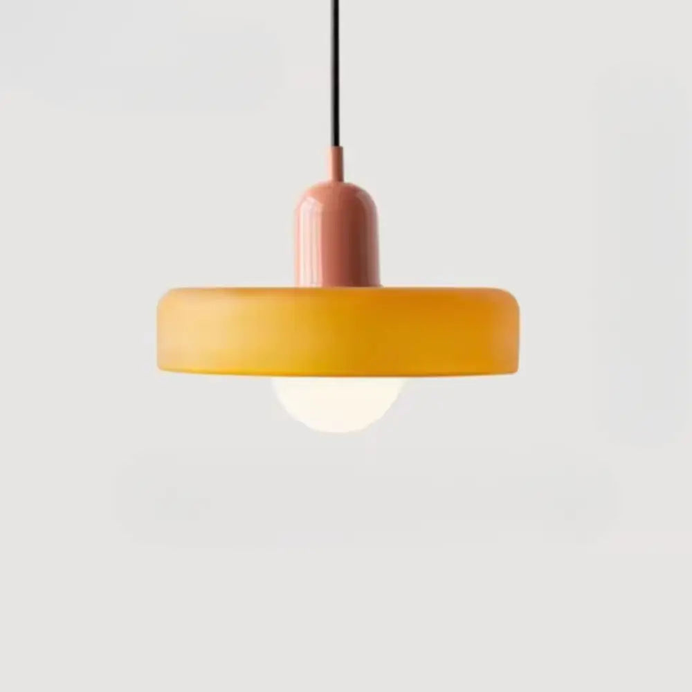 A bauhaus style glass pendant lighting with a matte peach cylindrical stem and amber glass pendant shade suspended by black cord