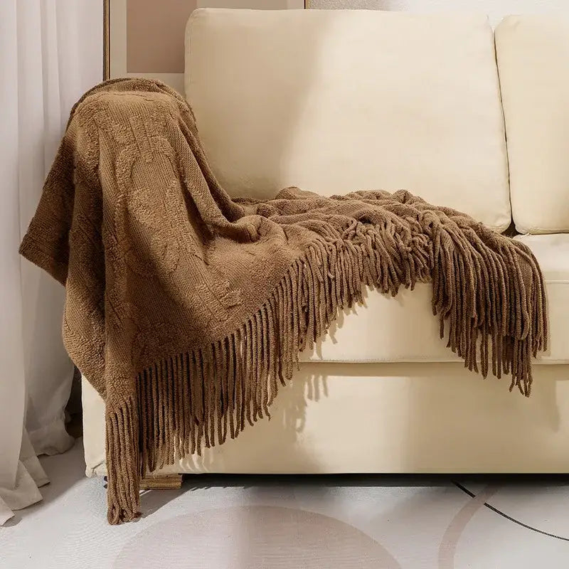 A cozy earthy-brown decorbites knit blanket with cable pattern and fringe drapes over a cream sofa for knit blanket sofa decor