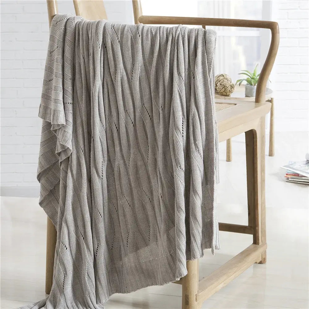 A soft light gray decorbites bamboo knitted cooling blanket with textured cable pattern draped over wooden chair