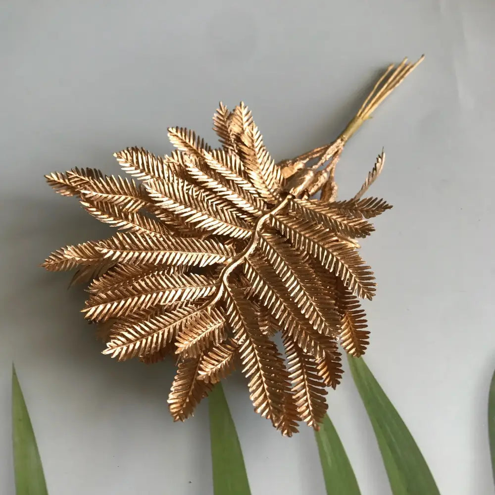 Golden metallic fern brooch with intricate leaf detailing displayed alongside artificial eucalyptus leaf branches for living room decor