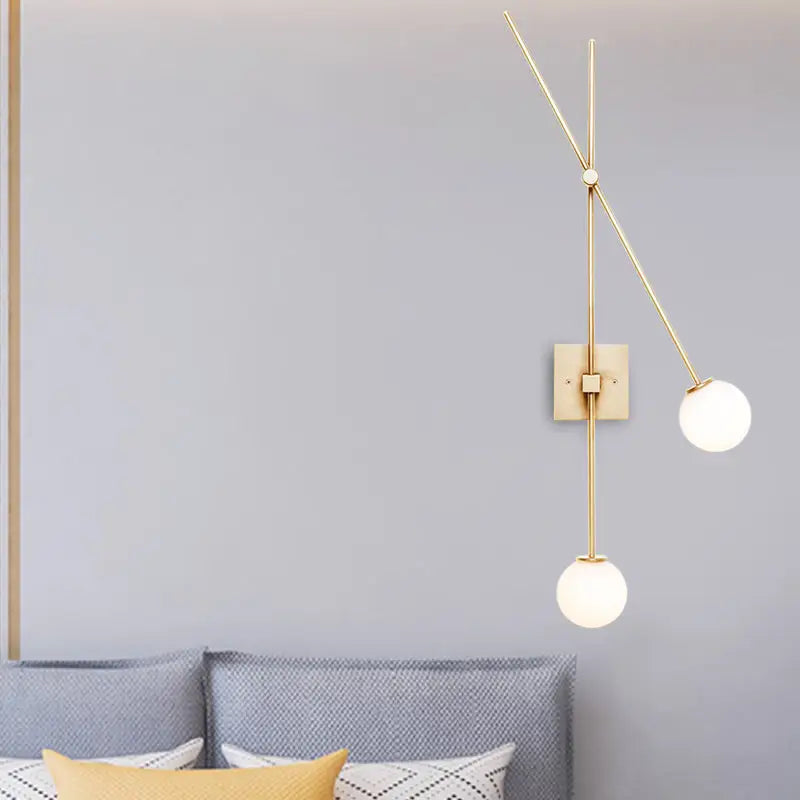 Gold-toned bedroom wall sconce light fixture with slender metal arms and two opal glass bubble frosted shades