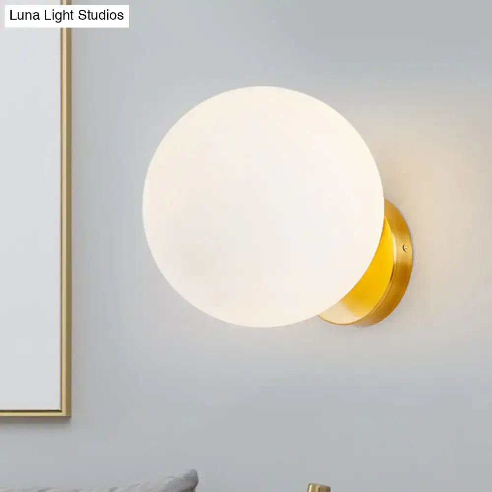 Minimalist gold and white bedroom wall sconce with a frosted white glass ball and polished metal base