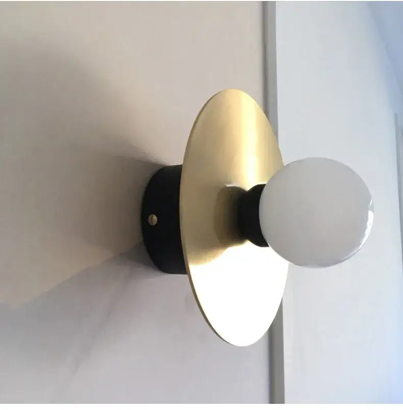 Modern black and brass glass ball wall light fixture with sleek base gold-toned disc and frosted glass bulb decorbites golden glass