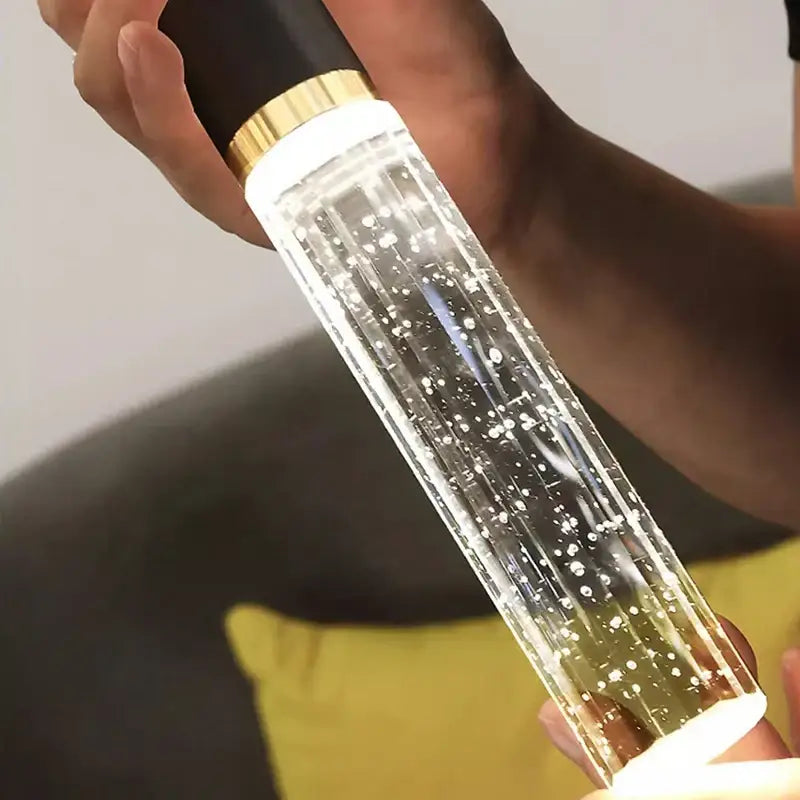 Clear cylindrical led light bottle with black and gold cap filled with glowing bubbles in decorbites crystal chandelier