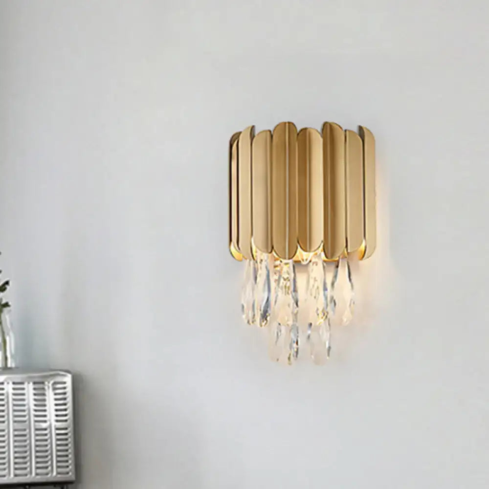 Gold-toned modern wall lamp with vertical leaf-shaped metal plates and clear crystal teardrop droplets for bedroom use