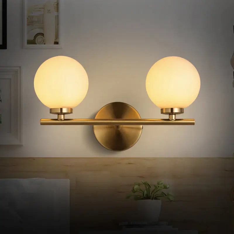 Modern brass bedroom sconce light fixture with gold-toned finish and two frosted glass product shade bulbs