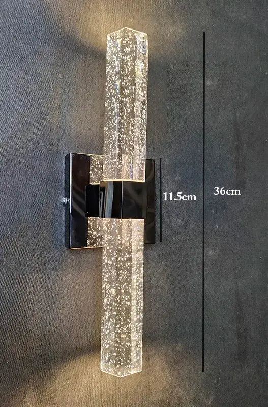 A modern black metal wall sconce with a clear bubble crystal led body filled with sparkling particles for bathroom mirrors