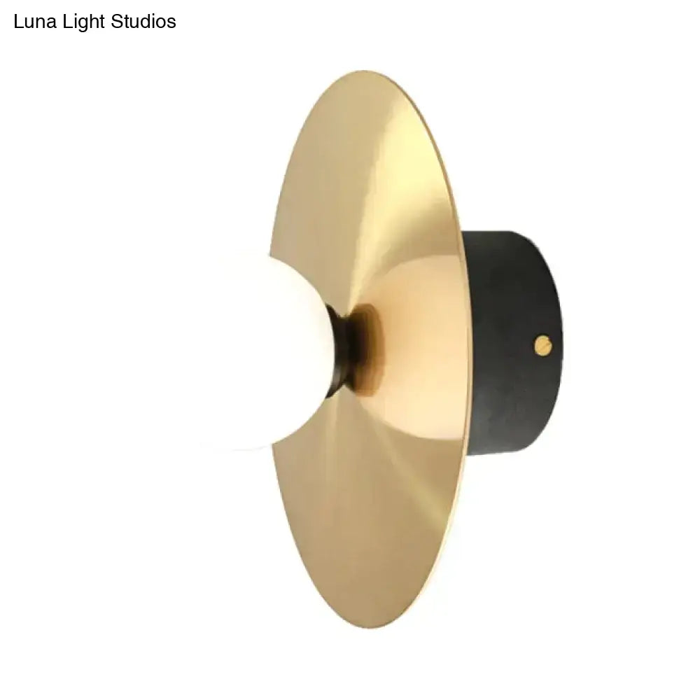 Modern gold and black riya wall light featuring a gold-toned brass disc, matte black base, and frosted glass bulb sconce