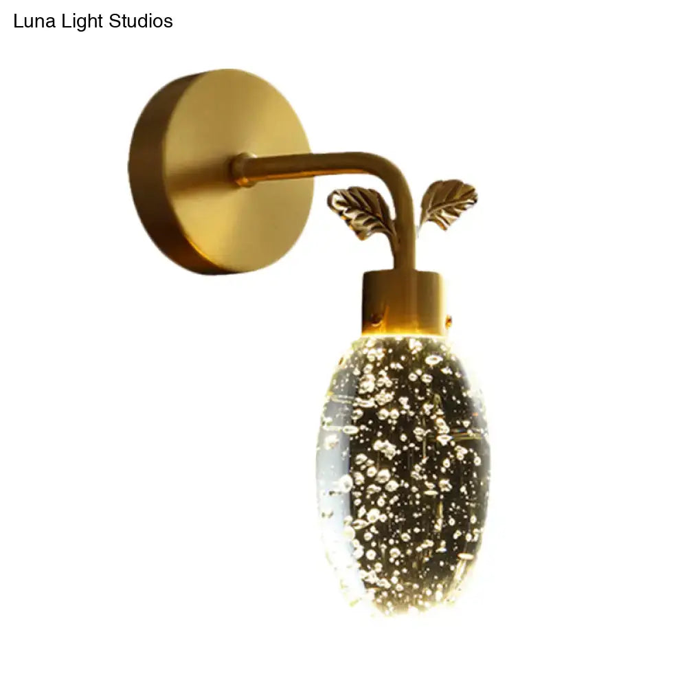 Modern gold led wall sconce with a seeded crystal globe filled with bubbles and leaf-shaped accents for bedroom use