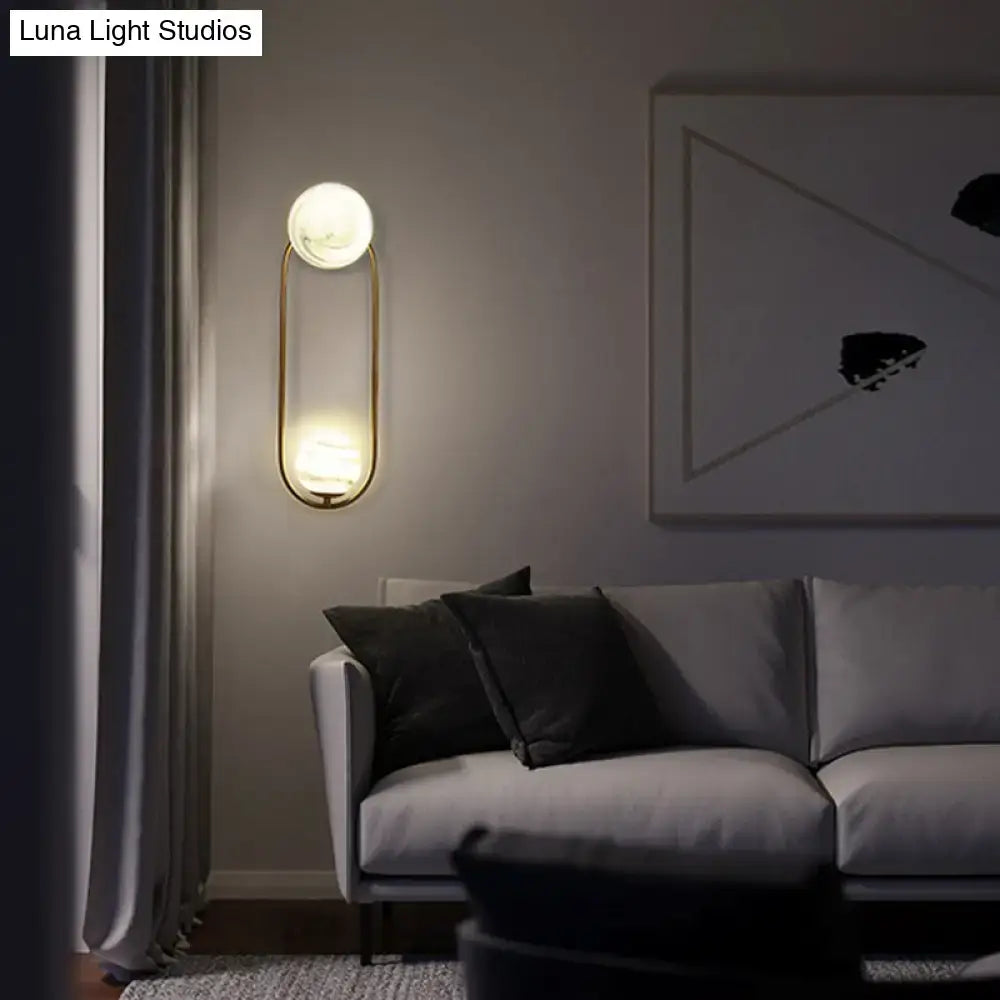 Modern gold oval wall sconce light fixture with frosted glass globe emitting warm light for living room use