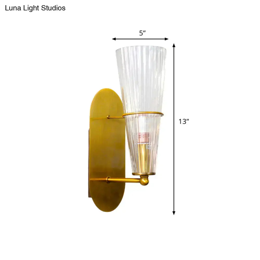 Modern gold wall sconce with clear vertically ribbed glass shade designed as a bedroom wall light