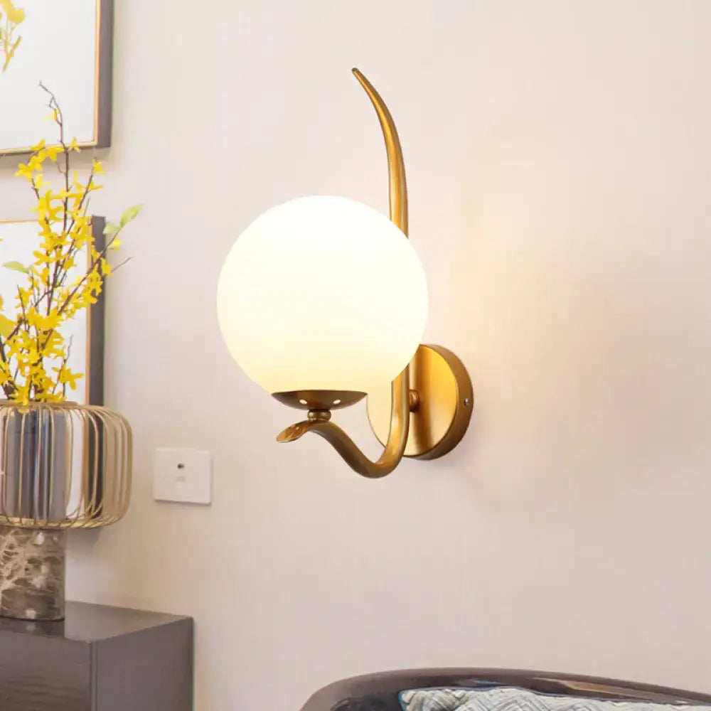 Modernist gold sconce light with white glass globe and curved metal arm suitable for 220v-240v use in bedroom