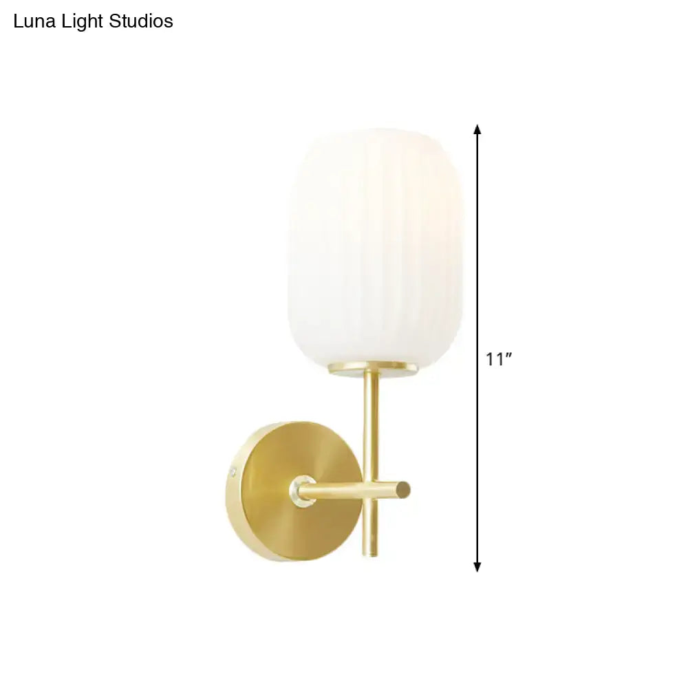 Gold-finished wall sconce light fixture with a vertically ribbed cream glass shade for bedroom use