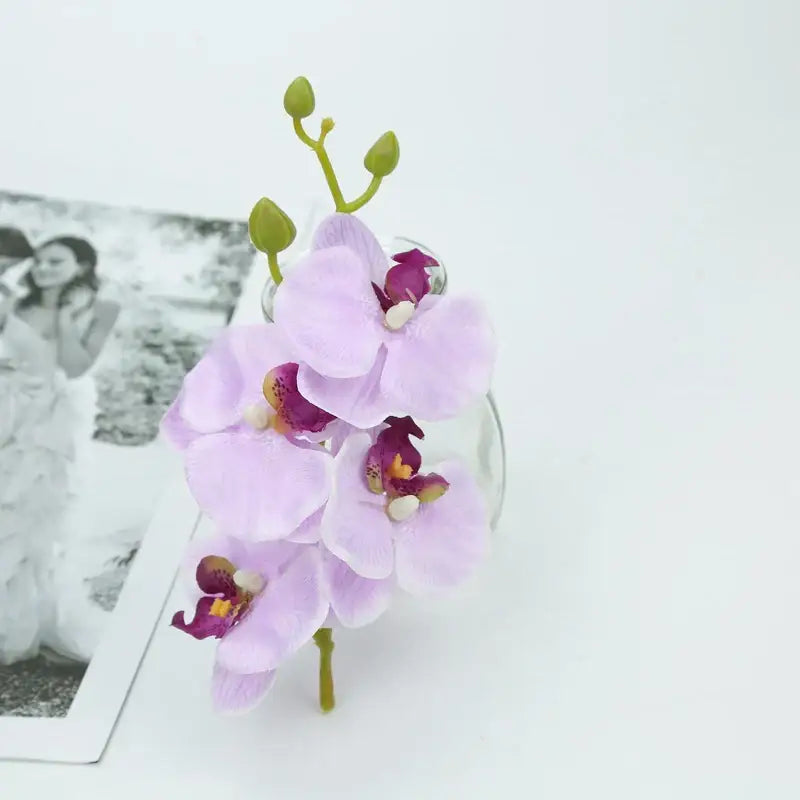 A vibrant silk butterfly orchid bouquet with delicate lavender petals and green buds in a clear glass vase for decor