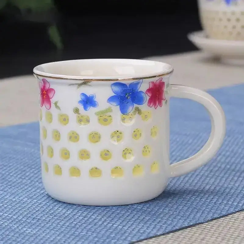 White ceramic tea cup with gold rim and colorful floral patterns above yellow perforated bowl from vintage cup set