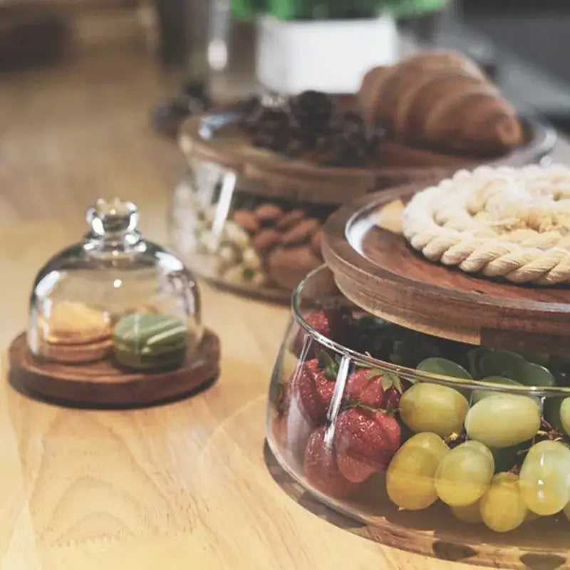 Three tier glass food storage containers with wood stand displaying two macarons under a transparent glass cover