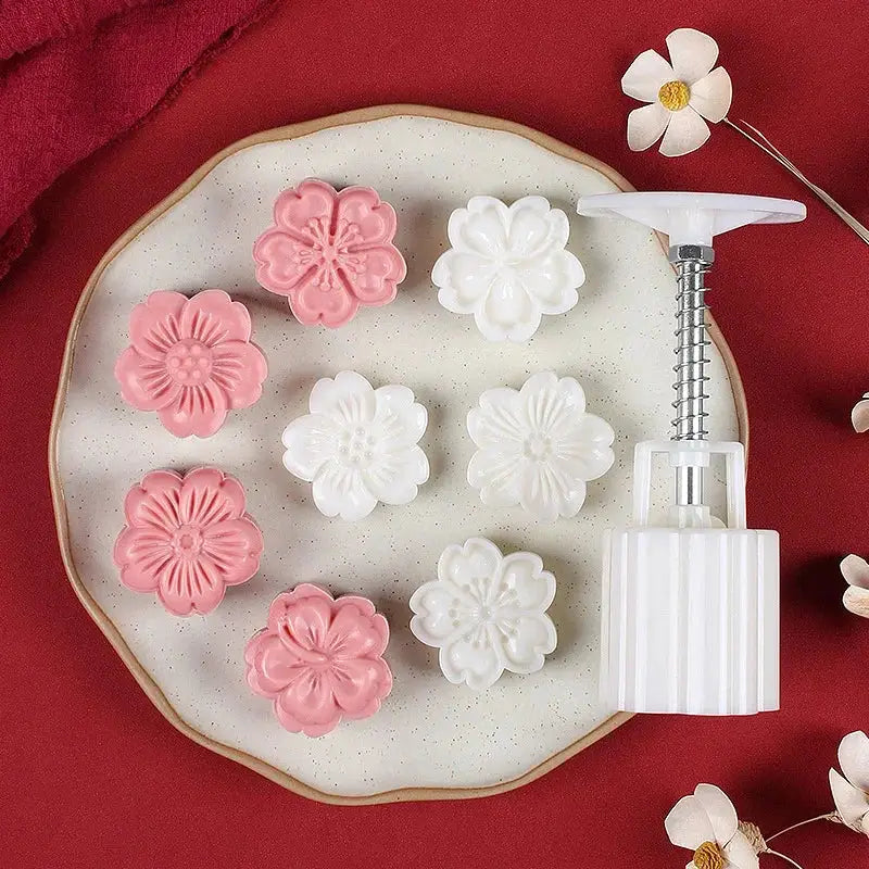 White and pink flower-shaped cherry blossom mooncakes on a speckled plate next to a white plastic decorbites 3d cherry mold