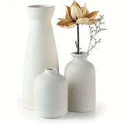 Set of three minimalist white ceramic vases with varying heights and one holding a dried golden lotus flower