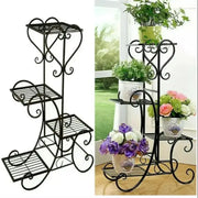 Black wrought iron metal plant stand with ornate scrollwork and four tiered shelves for indoor and outdoor display