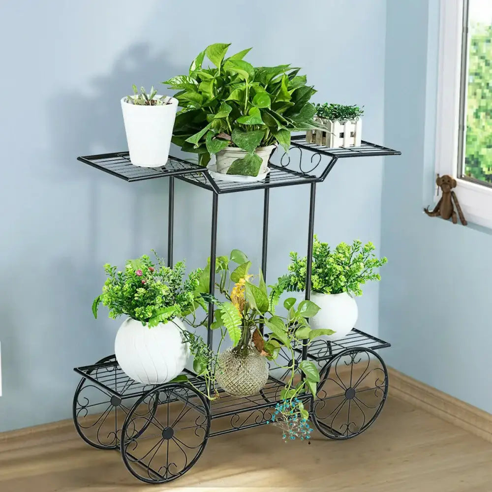 Black wrought iron metal plant stand with decorative wheels and three tiers holding potted green plants in white pots