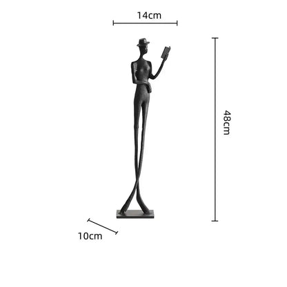 A sleek black metal decorbites human figure sculpture wearing a hat and holding a book for living room decor