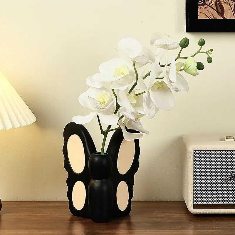 Black butterfly ceramic vase with cream oval cutouts holding white orchids for living room decorbites decor