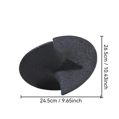 Black textured stone foot file with smooth curved surface and cutout alongside geometric ceramic gyroscope ornaments