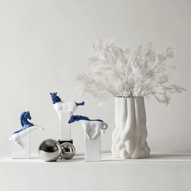 White ceramic vase with ribbed texture holding white dried foliage next to abstract black and gold decorbites horse statue