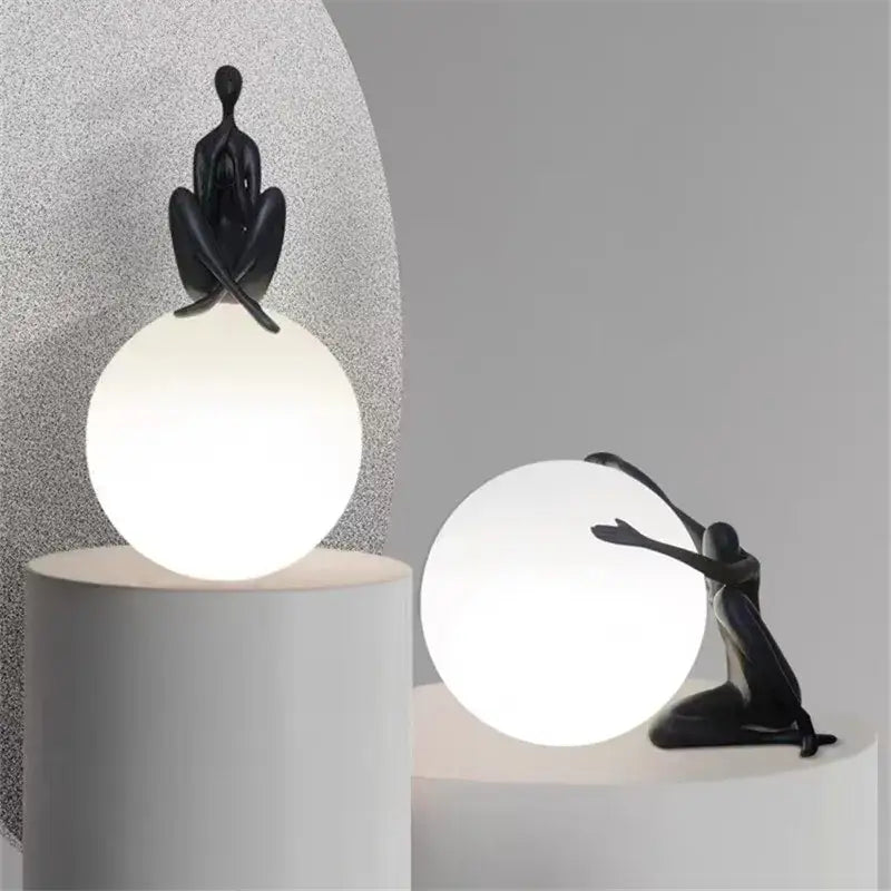Abstract black ball holding character resin lamp with red accents perched on glowing white spherical living room light