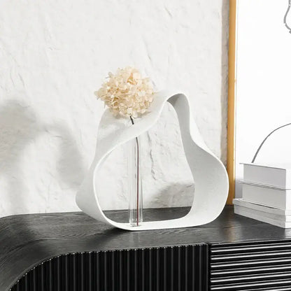 Abstract black resin ring sculpture featuring a white sculptural vase with glass stem and dried hydrangeas for home decor