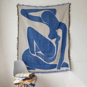 Beige throw blanket with bold blue abstract geometric knitted tassels and fringed edges hanging on wall