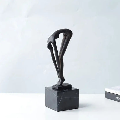 Black abstract diving sportsman metal sculpture of intertwined figures on dark marble base for living room decor