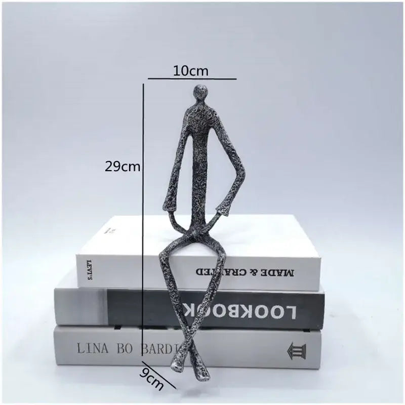 Abstract metal human sculpture with silver finish and elongated limbs seated on books for living room decorbites decor