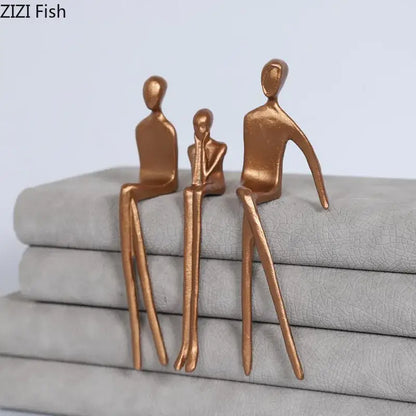 Bronze-colored abstract sculpture set with gold plated figure decor sitting on stacked gray fabric for living room