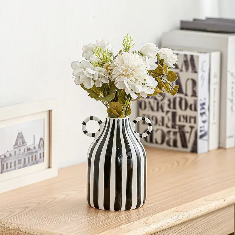 A sleek abstract ceramic hydroponic vase in black and white with double ear handles holding artificial white flowers