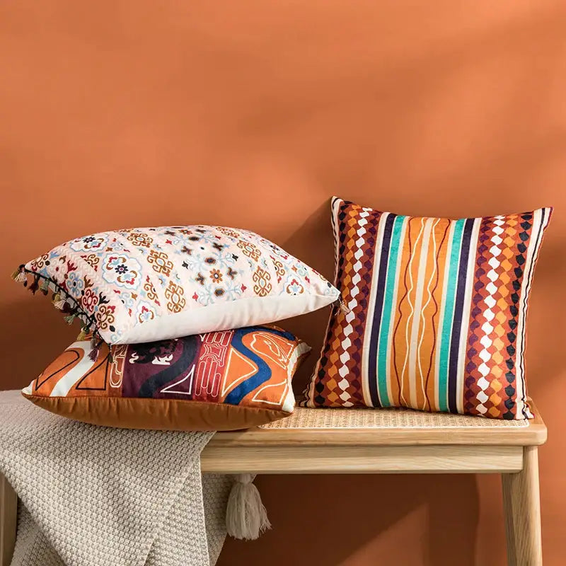 Three decorative cushion covers with abstract geometric embroidery in coral teal brown on wooden bench for decorbites abstract geometric decor