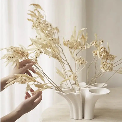 White fluted ceramic triple opening vase with abstract geometry design holding dried beige foliage for living room decor