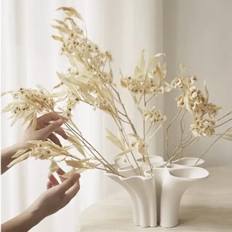 White fluted ceramic triple opening vase with abstract geometry design holding dried beige foliage for living room decor
