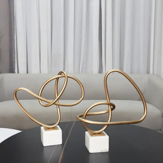 Two abstract gold line geometric metal sculptures with intertwined loops on white marble bases for living room decorbites decor