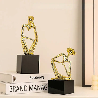 Two abstract gold figurines seated on black bases for decorbites golden hat thinker living room decor