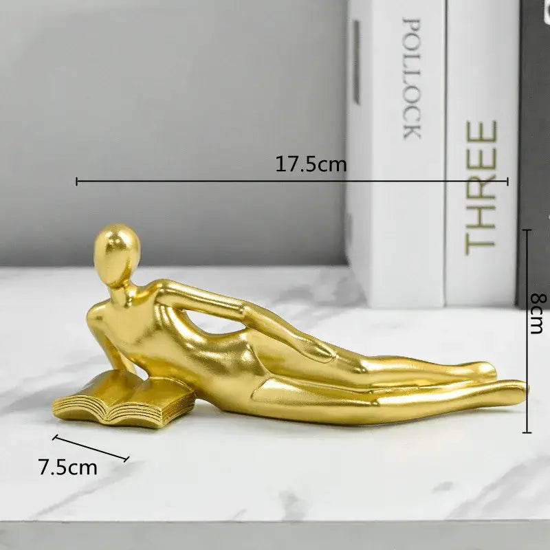 Golden metallic thinker reader figurine of a reclining man on an open book ideal for living room decor
