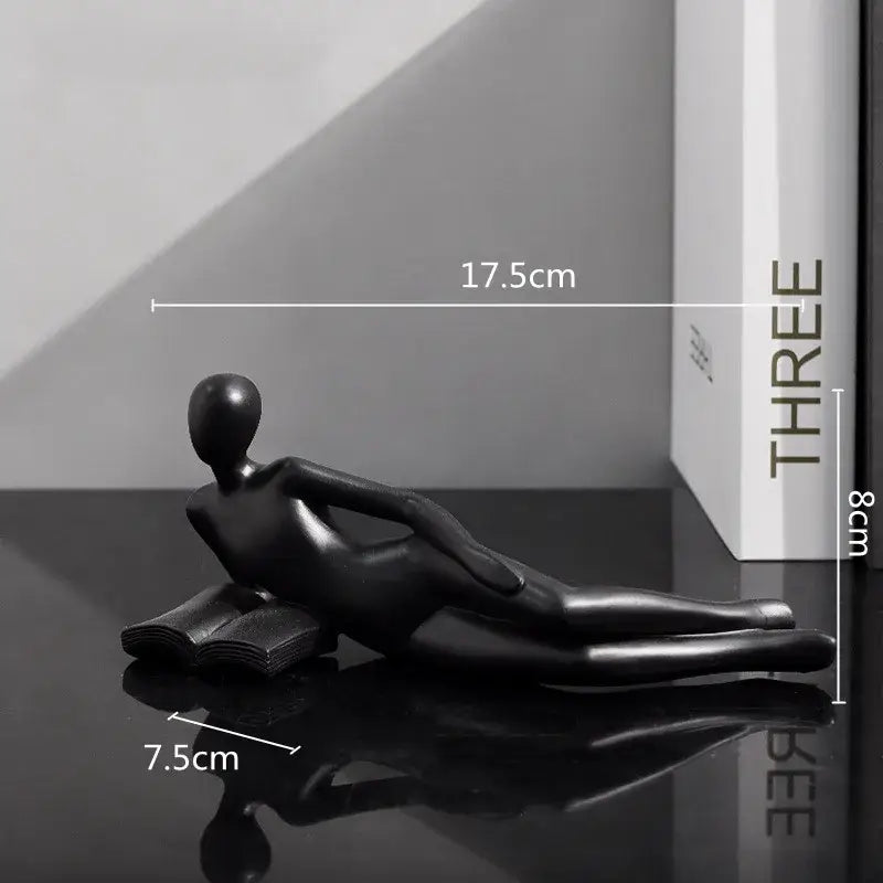Black glossy resin figurine of a reclining human form on an open book for abstract golden thinker reader decor