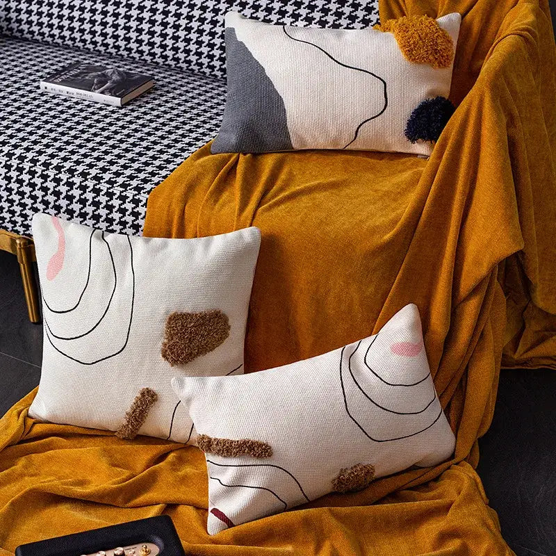 Cream-colored cushion cover with abstract line colors design and textured brown pom-poms by decorbites for living room decor