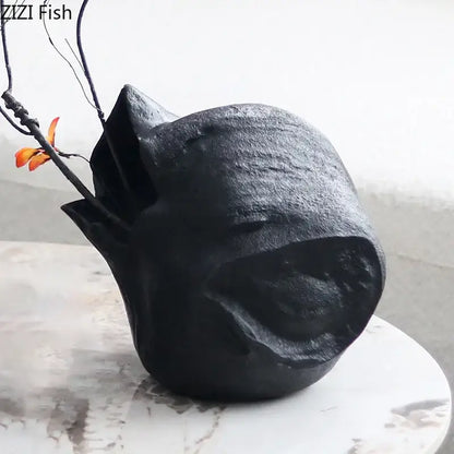 Abstract artwork black ceramic vase shaped like a stylized fish holds orange flowers for living room decorbites black vase