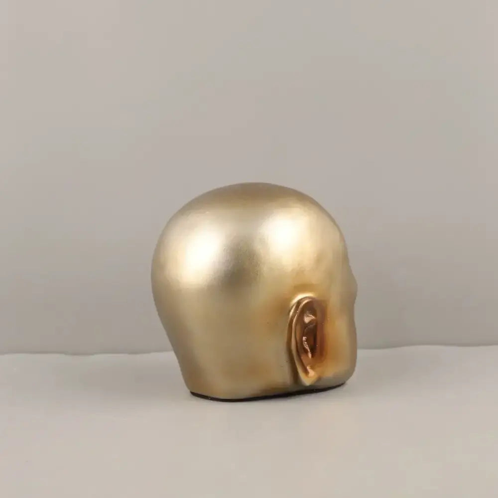 A smooth metallic gold-colored skull-shaped decorbites golden head half sculpture with a detailed ear for home decor