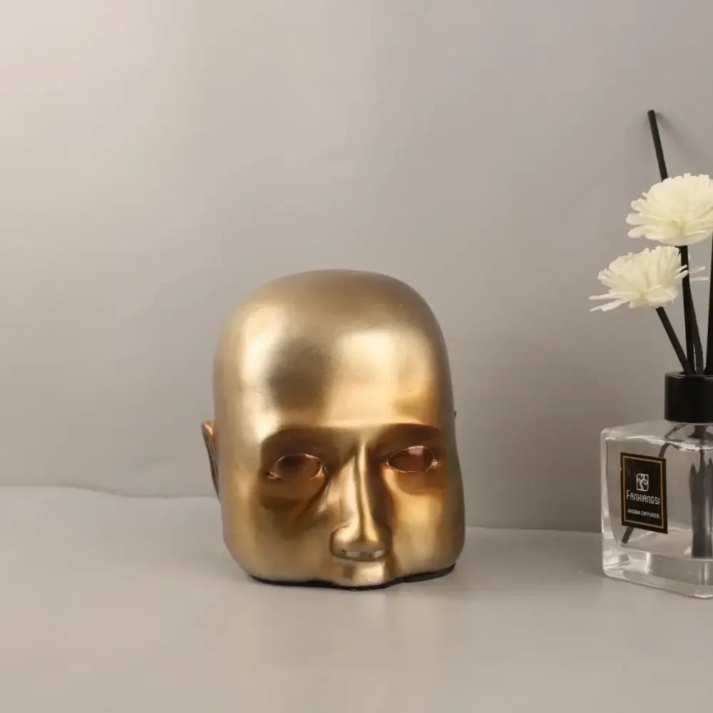 Golden metallic sculpture of a minimalist bald human head with smooth reflective surface for home decor decorbites golden head